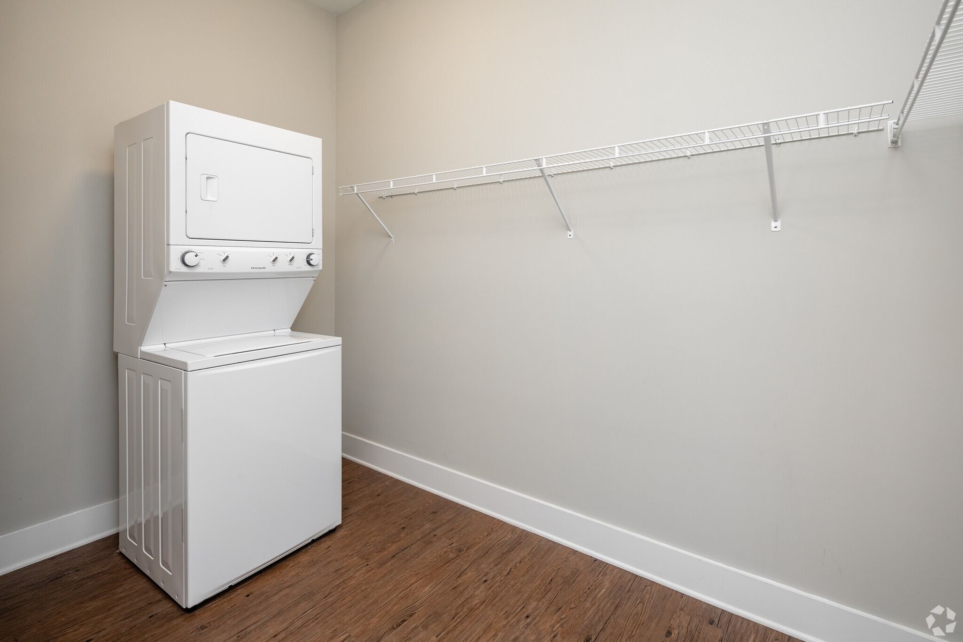 White stacked washer and dryer in a compact laundry closet with a wire shelf.
