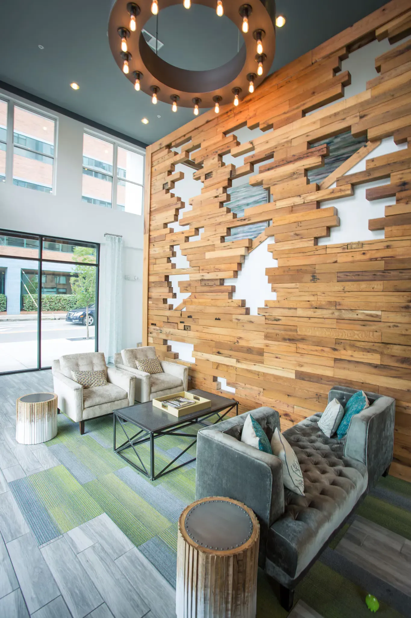 Interior of a modern apartment lobby with a wood feature wall, seating, and a circular chandelier.