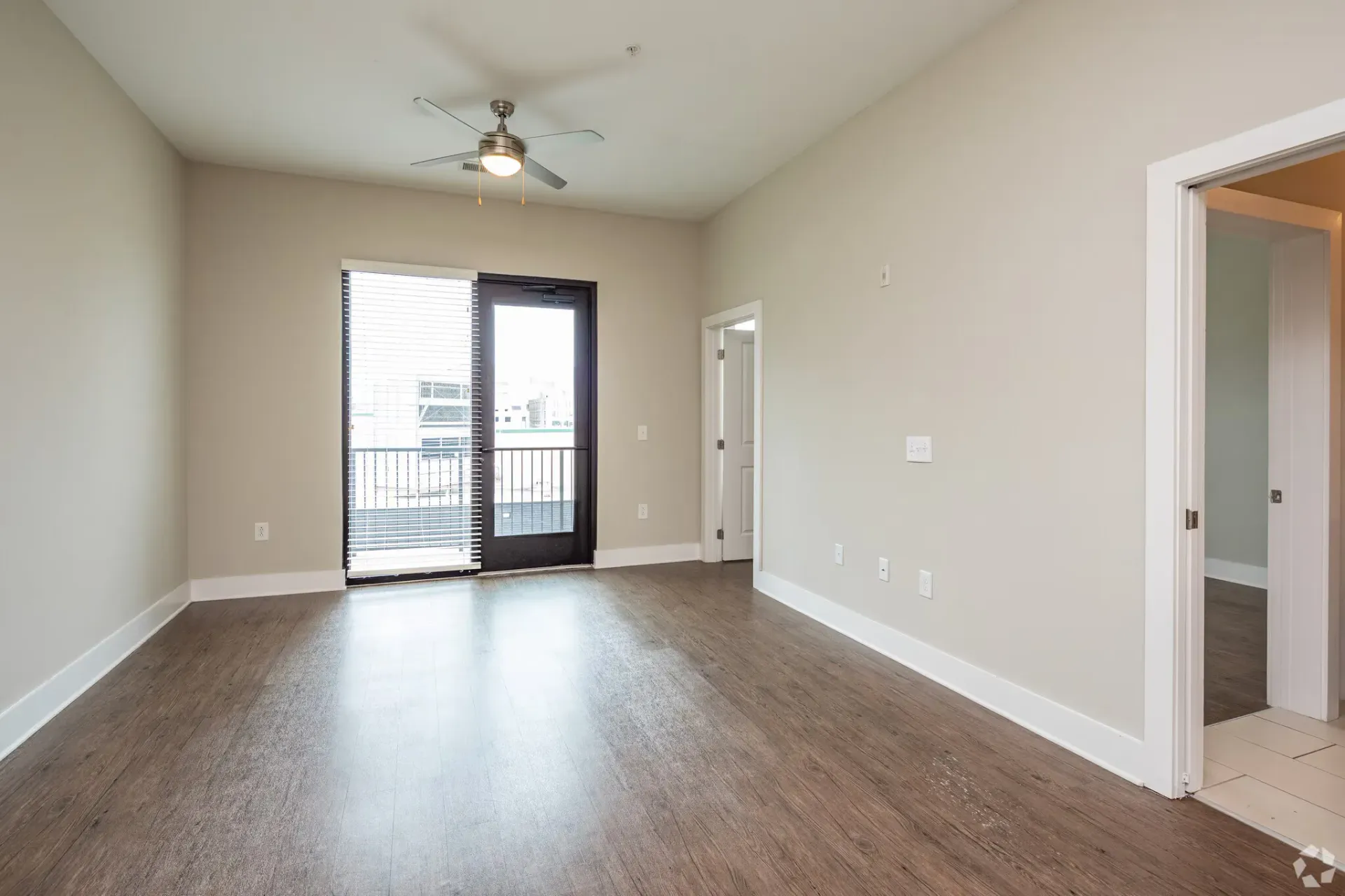 Empty living room with balcony door, blinds, and a ceiling fan.