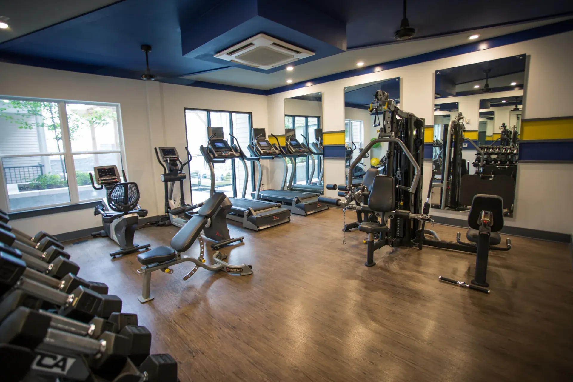 Well-equipped gym with cardio machines, weight machines, dumbbells, and mirrors.