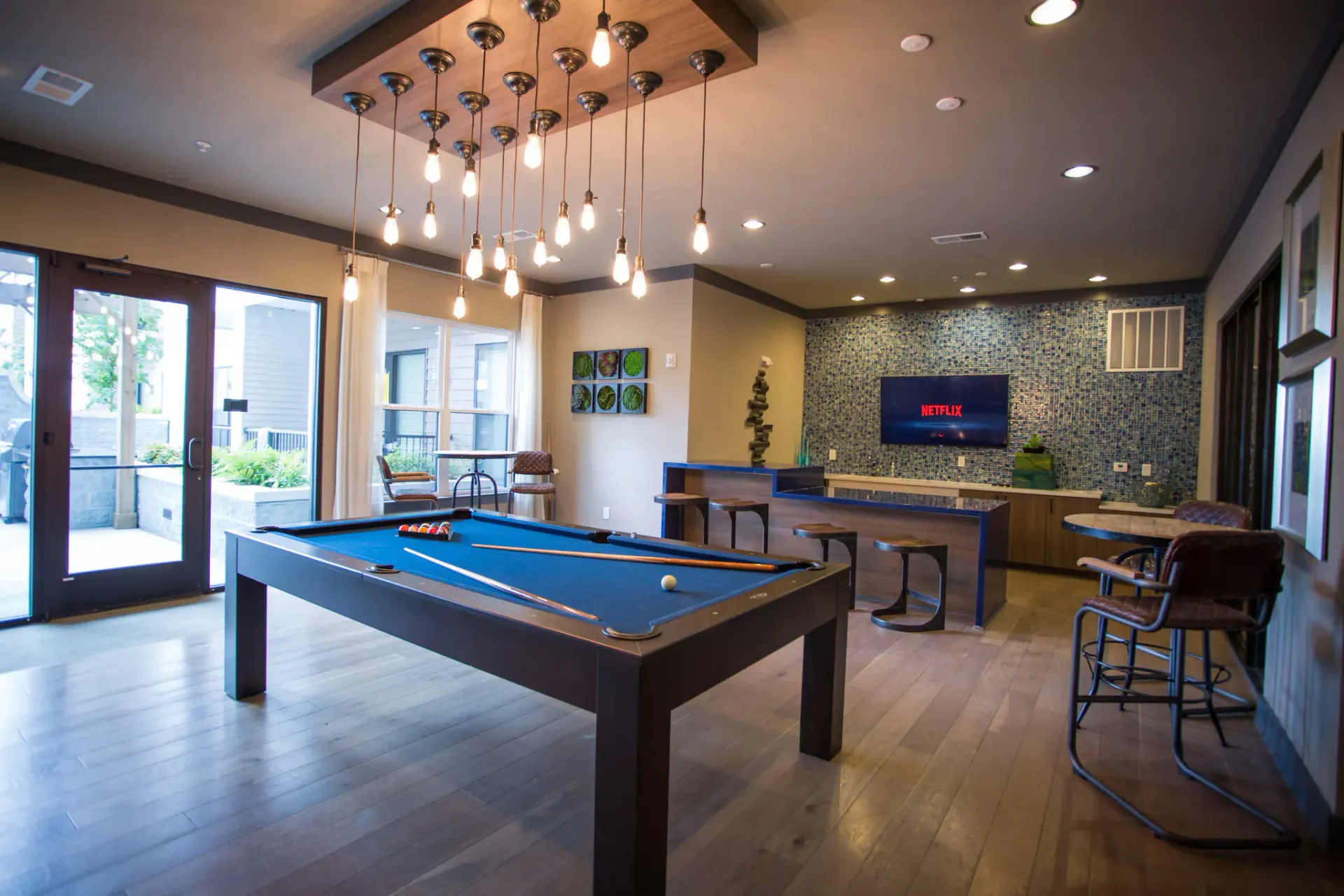 Indoor community lounge with a pool table, bar stools, and a wall-mounted TV.