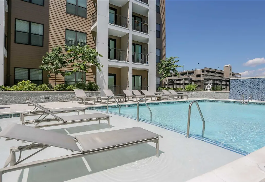Outdoor pool area at an apartment community with lounge chairs and building balconies.