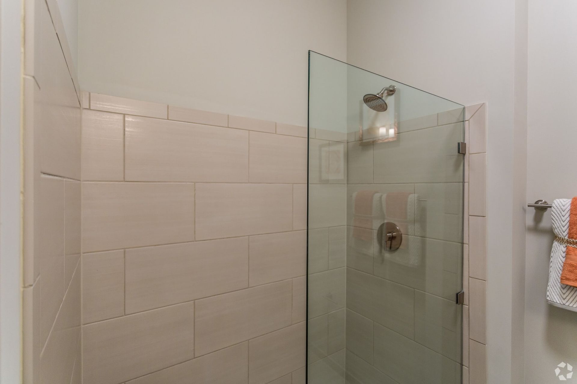 Walk-in shower with frameless glass door, beige tile walls, and a wall-mounted shower control.