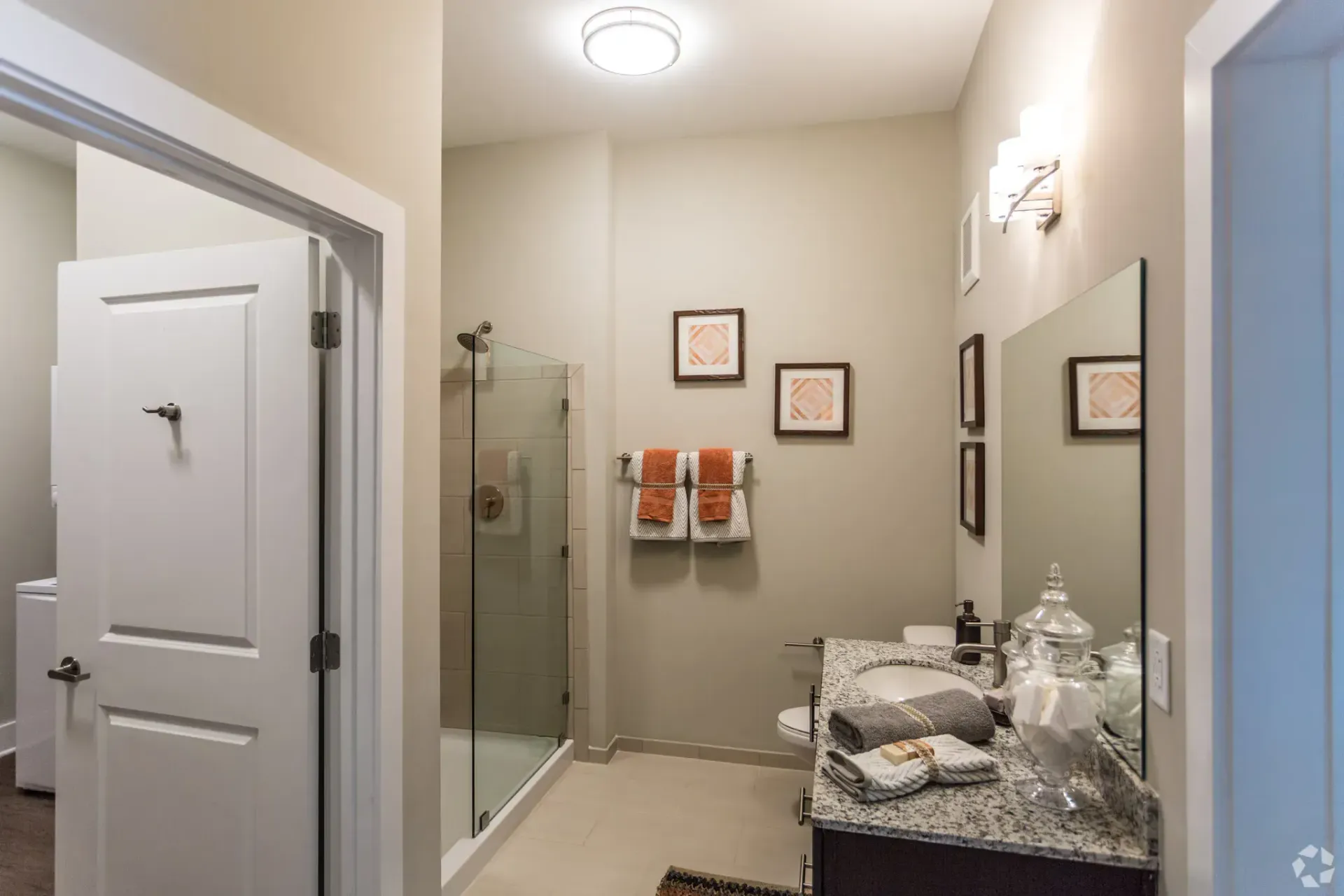 Bathroom in an apartment with a glass-enclosed shower, granite vanity, and folded towels on the counter.