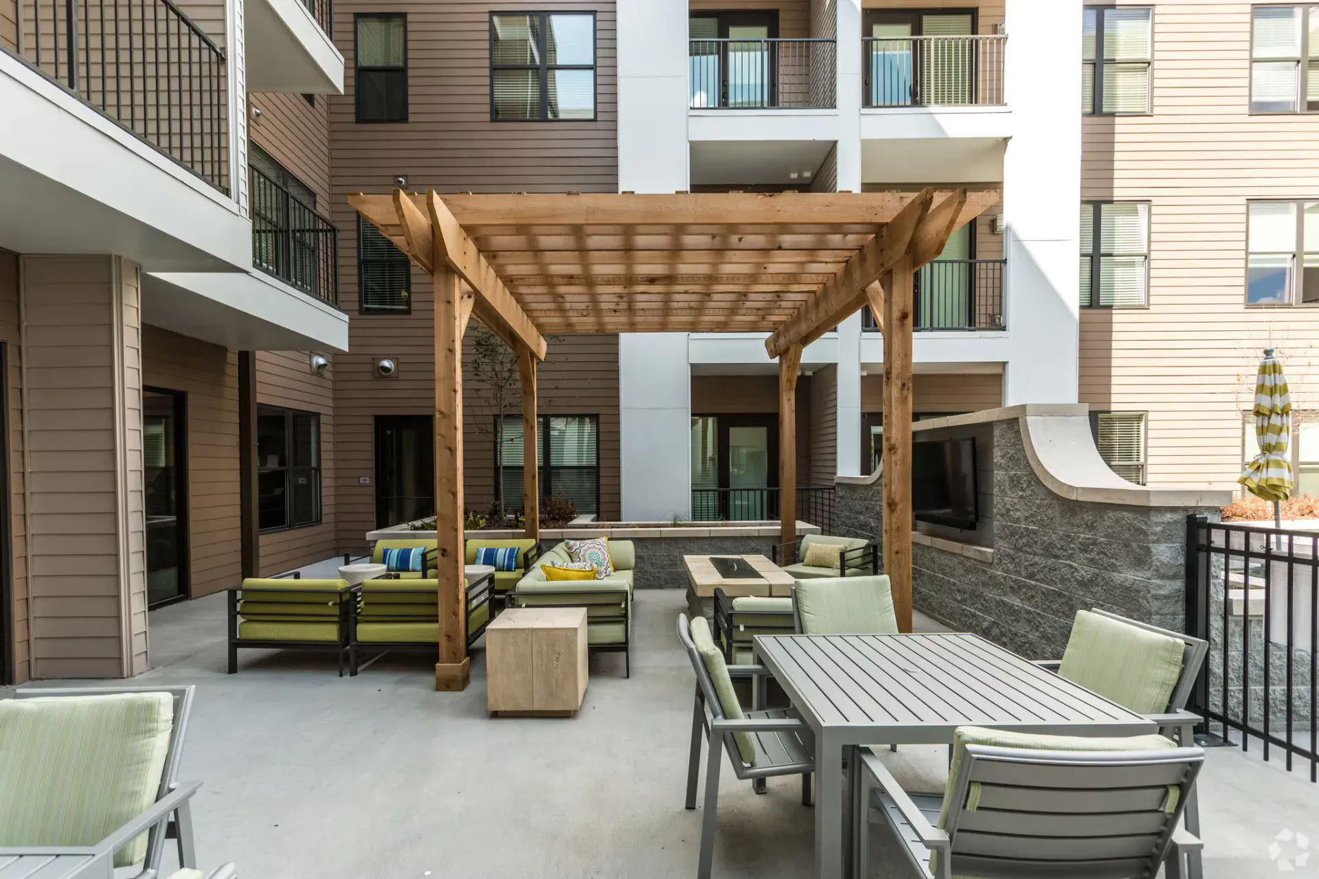 Outdoor communal courtyard with a wooden pergola, lounge seating, and a dining table.