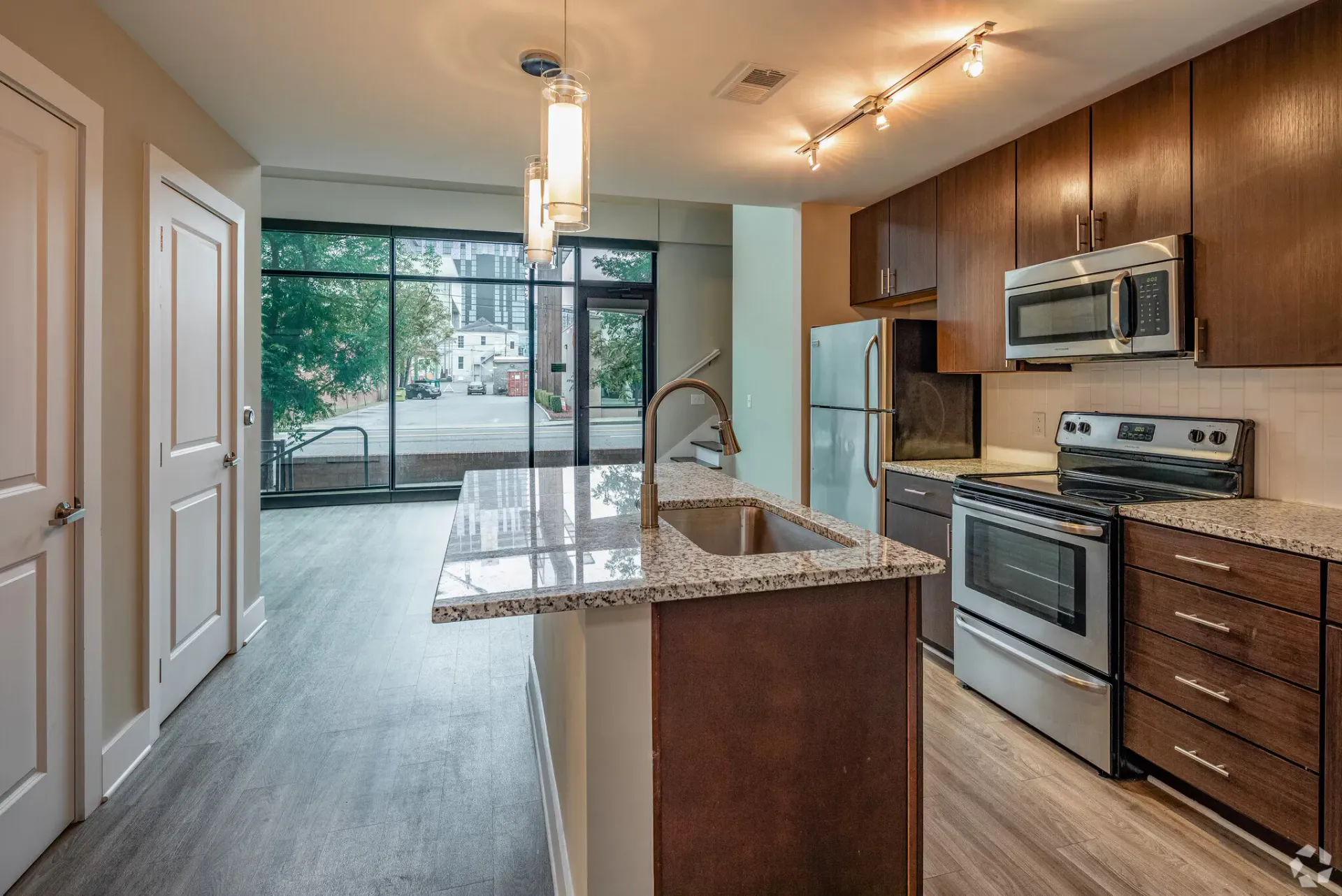 Modern apartment kitchen with granite island, sink, and stainless steel appliances.