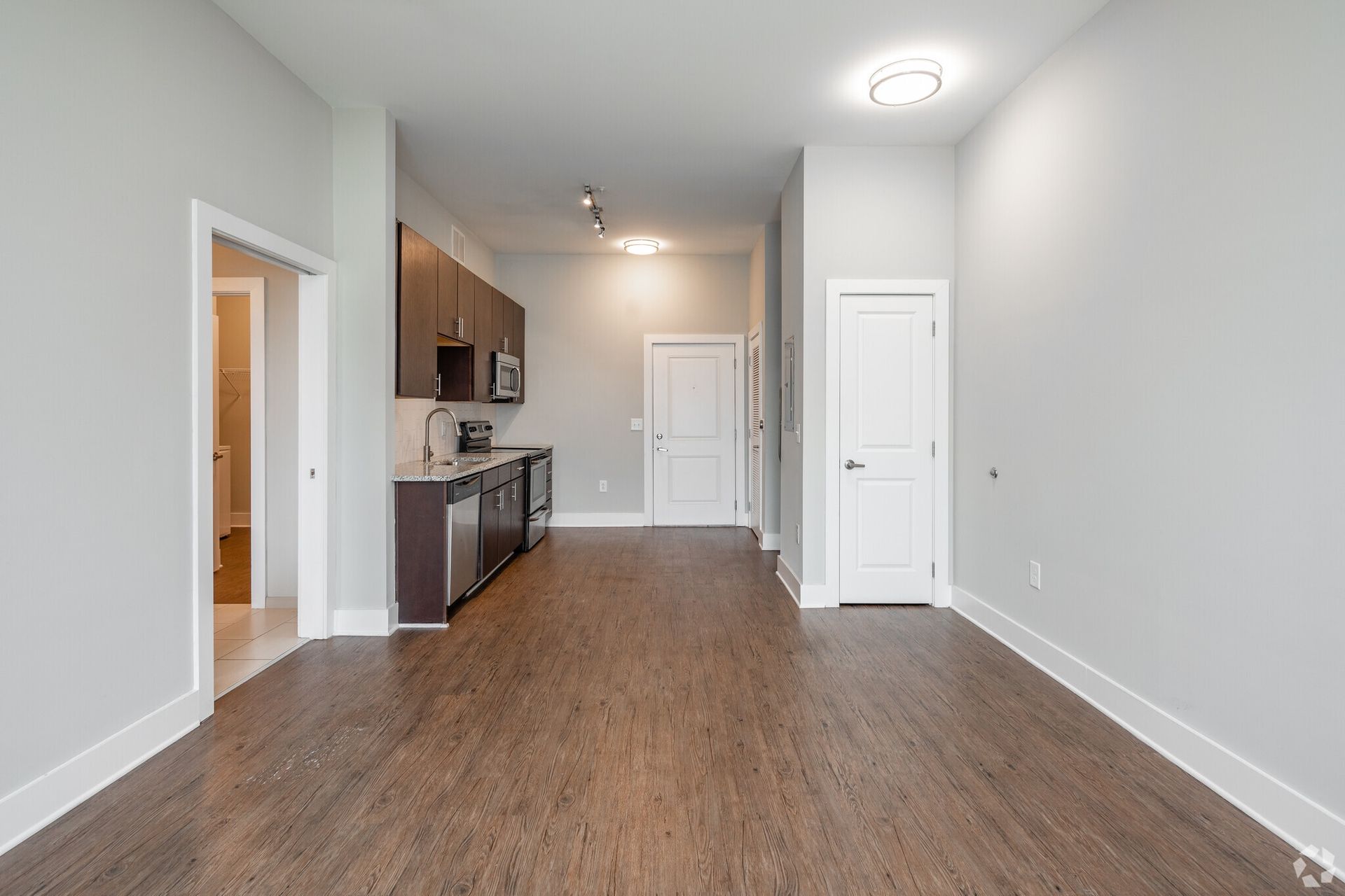 Open-plan kitchen in apartment with dark cabinets, stainless appliances, and wood-look flooring.