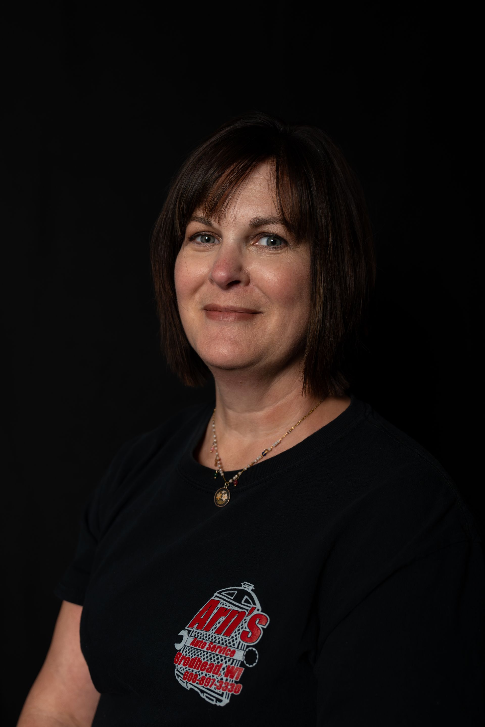 Man with glasses, shaved head, black shirt with logo, smiling against black background.  | Arn's Auto Service