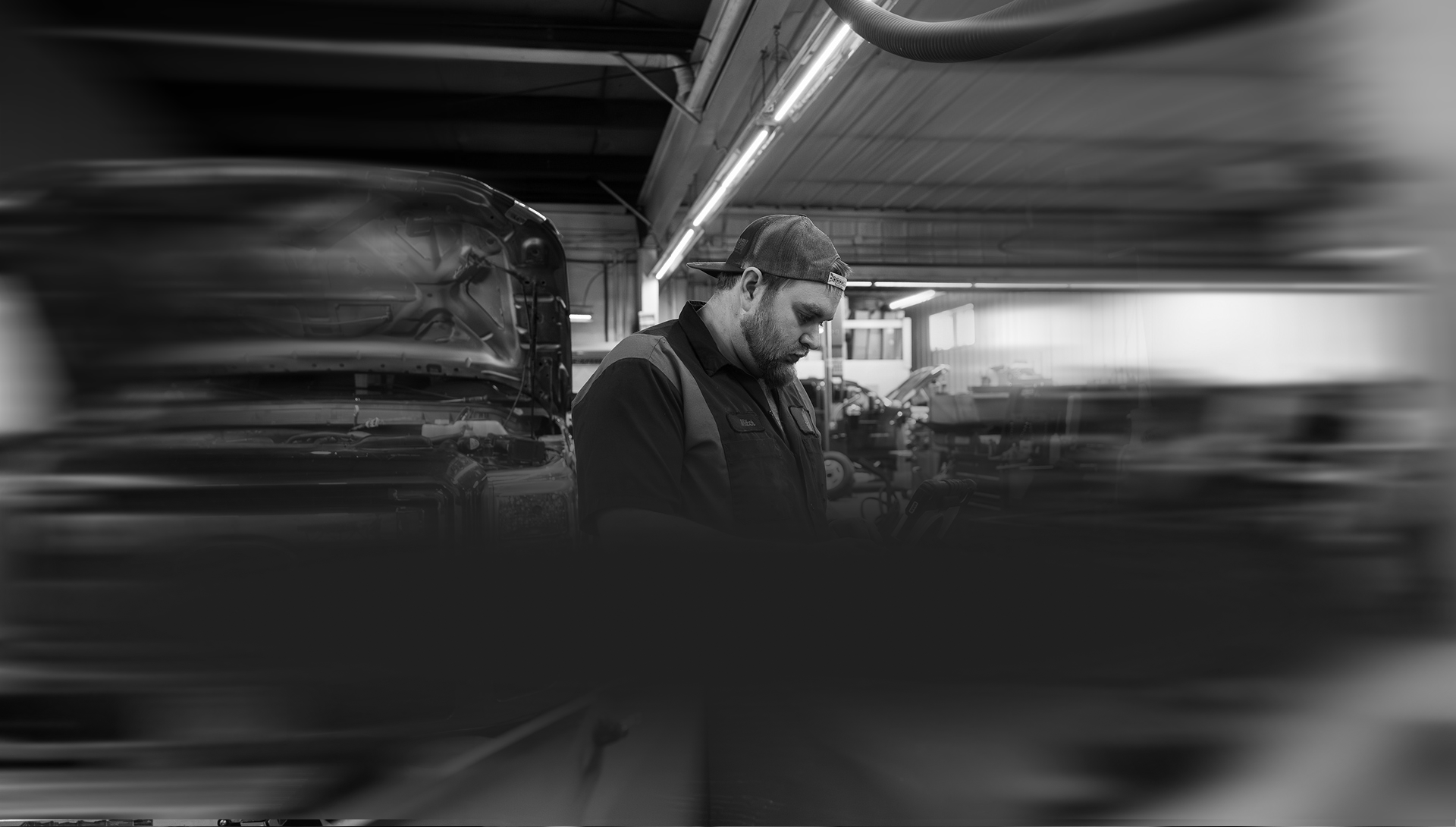 Man working in a workshop, wearing a cap, focused. Black and white photograph. | Arn's Auto Service