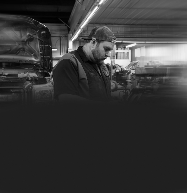 Mechanic in a cap working on a vehicle in a garage. | Arn's Auto Service