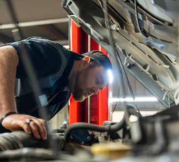Mechanic inspecting car engine with headlamp in auto shop. | Arn's Auto Service