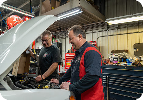 Two mechanics, one smiling, examining a car engine in a garage | Arn's Auto Service