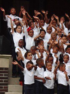 A large group of children are raising their hands in the air