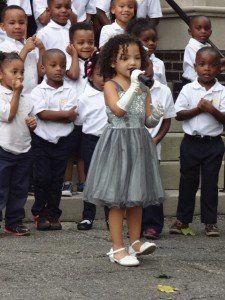 A little girl singing into a microphone in front of a group of children