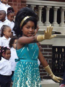 A little girl in a blue dress and gold gloves