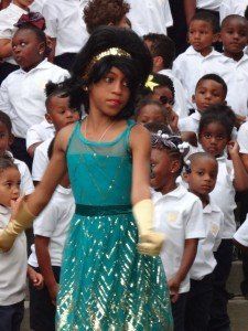 A girl in a blue dress is standing in front of a crowd of children