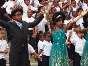 A boy in a suit and tie is standing in front of a crowd of children