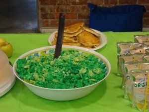 A bowl of green rice is on a table next to pancakes.