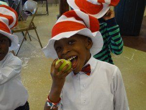 A boy wearing a cat in the hat hat is eating an apple