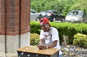 A man is sitting at a desk with a brick wall in the background.
