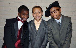 Three young boys are posing for a picture while wearing suits and ties