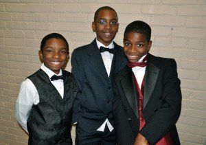 Three young boys wearing tuxedos and bow ties are posing for a picture.