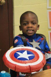 A young boy dressed as captain america is holding an inflatable shield
