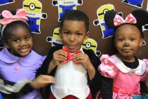 A boy and two girls are posing for a picture in front of a wall with minions on it.