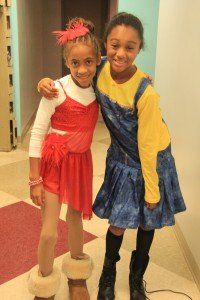 Two young girls are posing for a picture in a hallway.