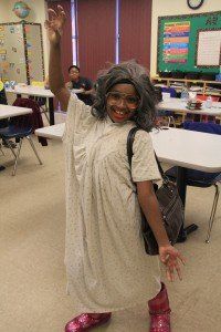 A young girl dressed as an old woman is standing in a classroom.