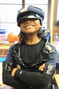 A young boy wearing a hat and a black shirt is smiling with his arms crossed