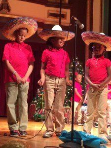 A group of children wearing sombrero hats are singing into a microphone.