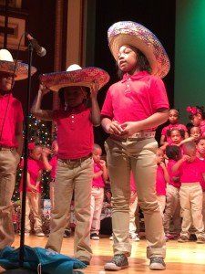 A group of children are standing on a stage wearing sombrero hats.