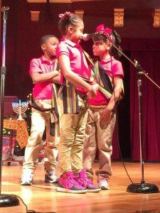 A group of children are singing into microphones on a stage.