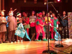 A group of children dressed in christmas costumes are standing on a stage in front of a microphone.