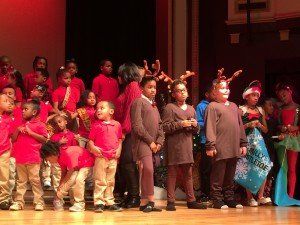 A group of children are standing on a stage wearing reindeer antlers.