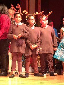 A group of children dressed as reindeer are standing on a stage.