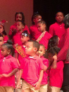 A group of children in red shirts are standing on a stage.