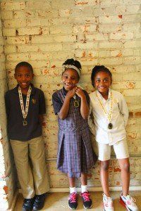 A boy and two girls are standing next to each other in front of a brick wall.