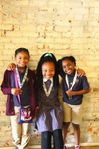 Three young girls are posing for a picture in front of a brick wall.
