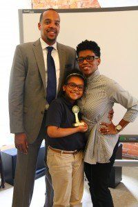 A man in a suit and tie is standing next to a woman and a boy holding a trophy.