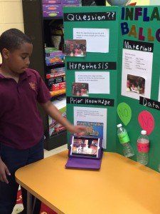 A boy is standing in front of a green board that says 