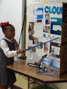 A little girl stands in front of a poster that says clouds