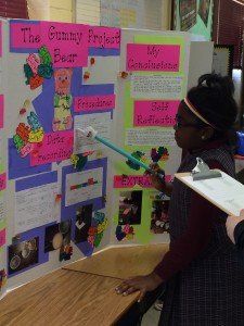 A girl is pointing at a board that says the gummy bear project
