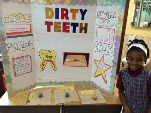A little girl is standing in front of a poster that says dirty teeth