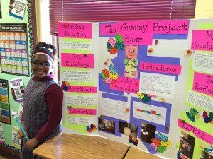 A young girl is standing in front of a project board in a classroom.