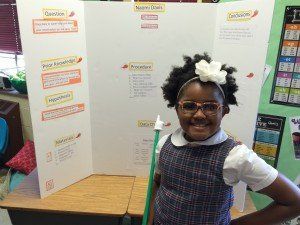 A young girl is standing in front of a presentation board in a classroom.