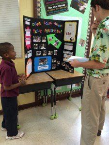 A man is standing next to a boy in front of a project board.