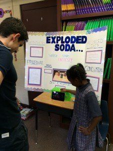 A man and a girl are standing in front of a poster that says exploded soda.