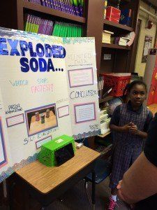 A girl is standing in front of a poster that says ' exploded soda ' on it.